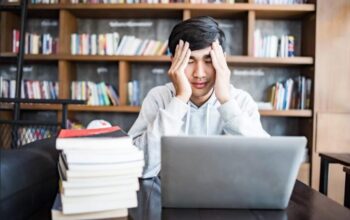 Mahasiswa belajar dengan tumpukan buku dan laptop